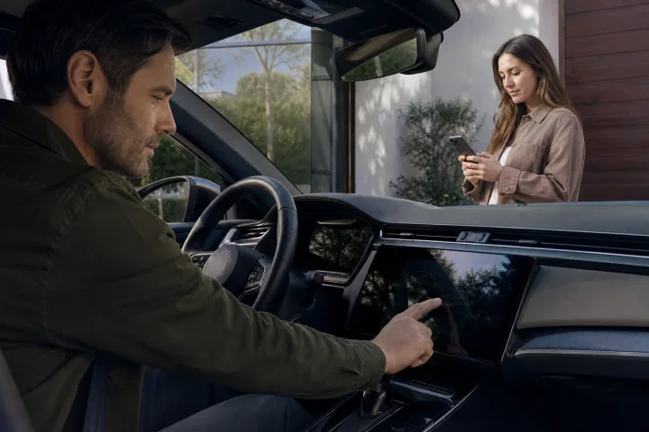 Una persona revisa la pantalla central y la aplicación móvil de un coche antes de entregarlo a otro propietario.