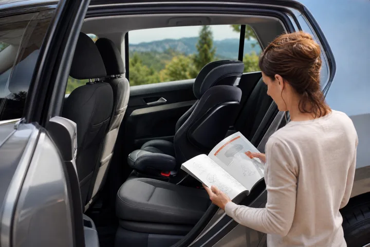 Adulto consultando el manual de un coche junto a una silla infantil colocada en un asiento trasero