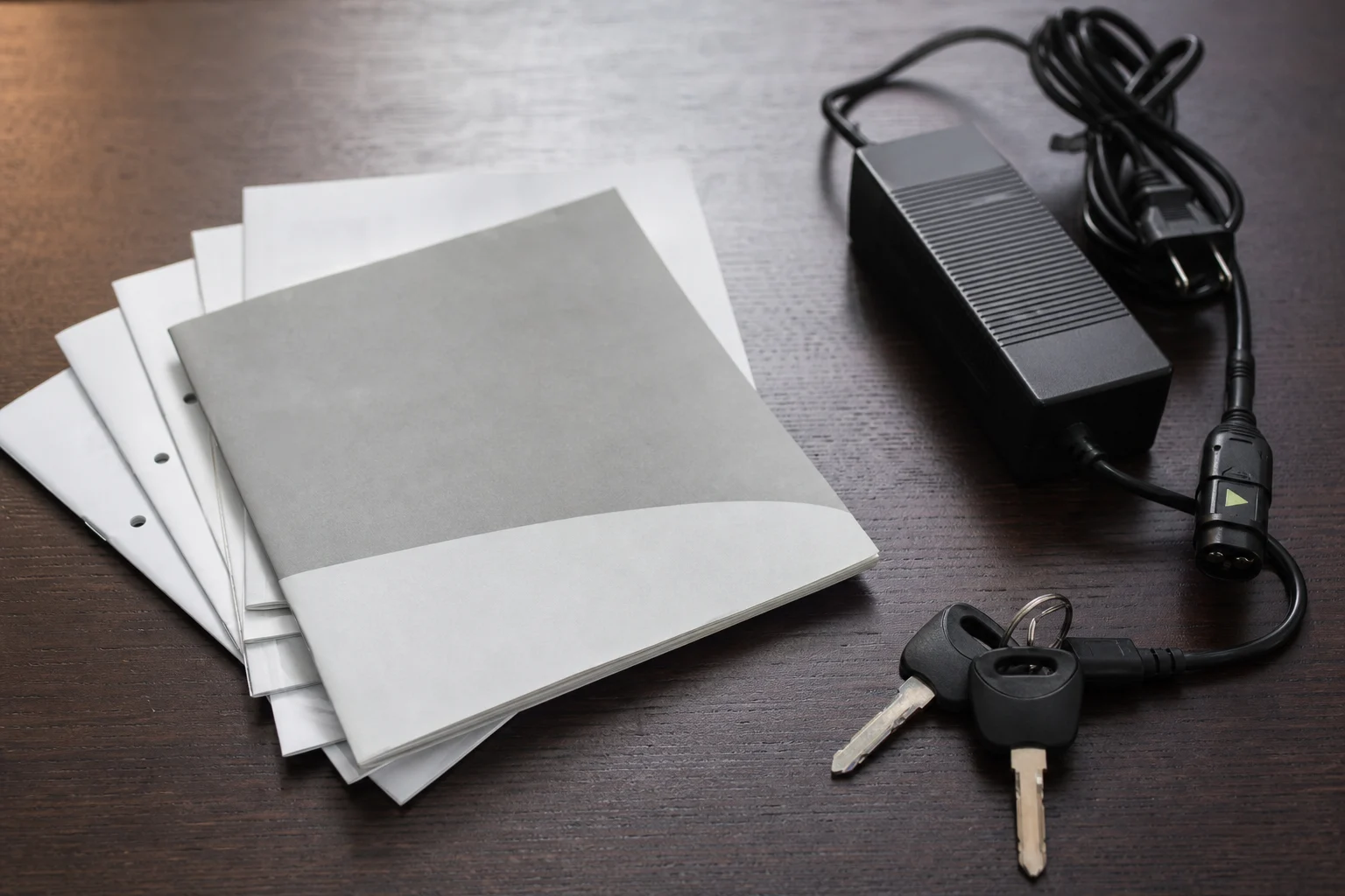 Unterlagen, Schlüssel, Ladegerät und Kabel eines gebrauchten Elektromotorrads auf einem Tisch